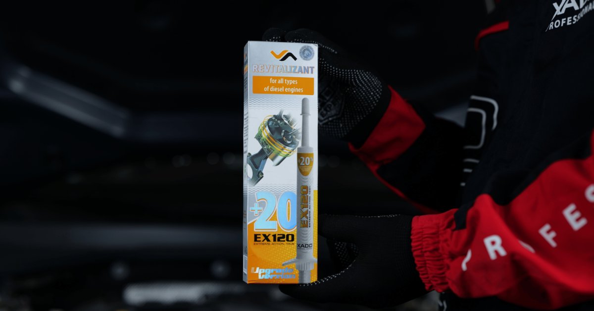 A close-up of a person wearing a black-and-red mechanic's suit, holding a box of a revitalizing product for vehicles.