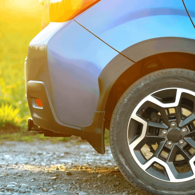 A low-angle view of a car parked on a gravel road near a grassy field, with a canister of XADO product placed near it.