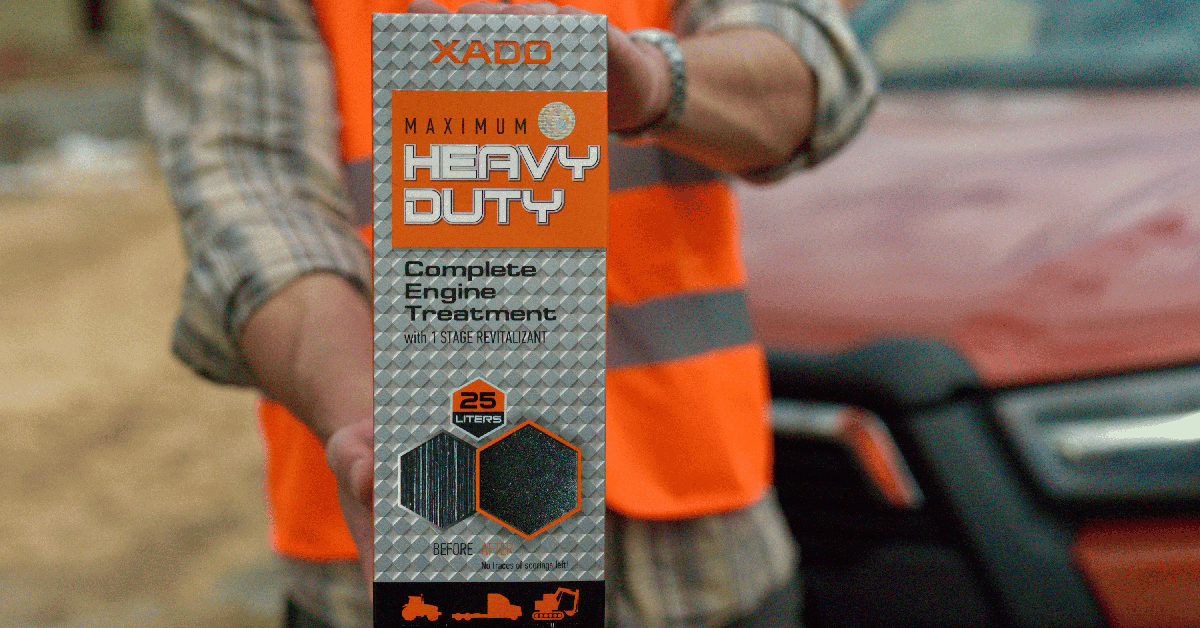 A close-up of a person wearing an orange construction safety vest, holding an engine treatment product box.
