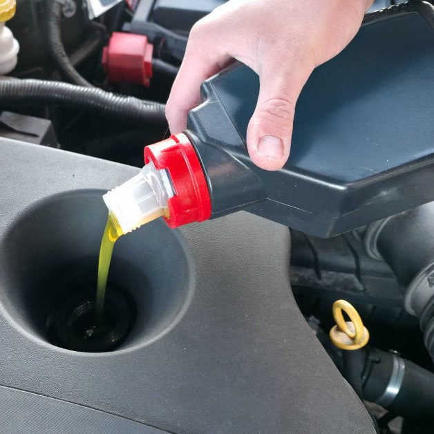 Technician pouring fresh motor oil into a vehicle engine during routine maintenance to support performance and engine protection.