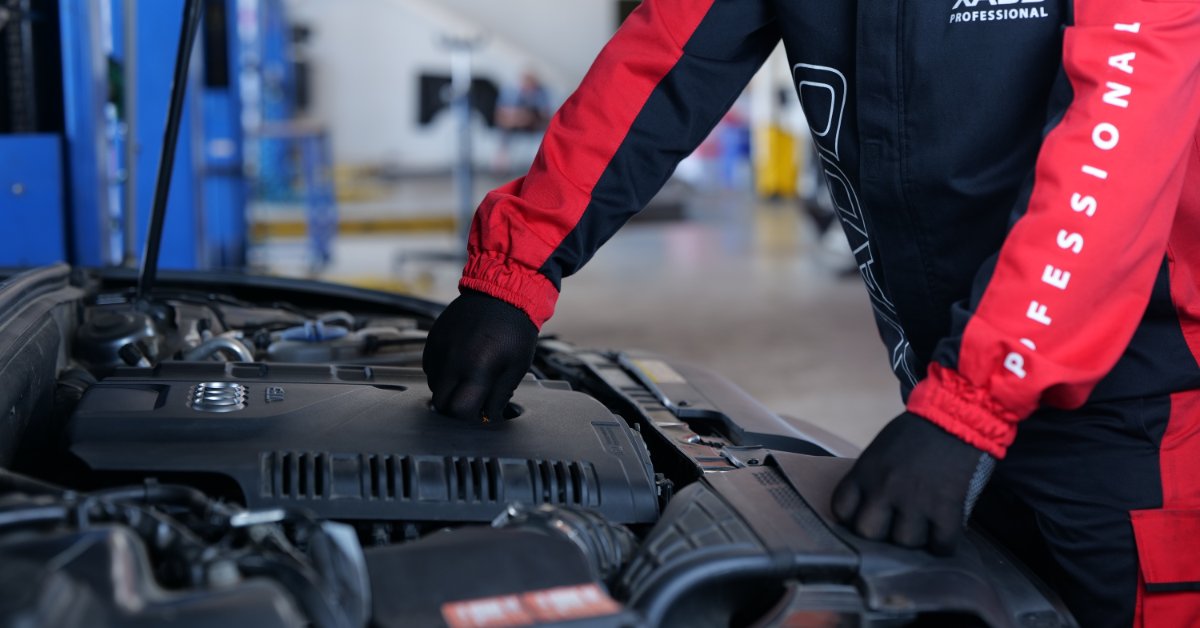 Automotive technician applying an engine treatment product during vehicle maintenance to support engine performance and protection.