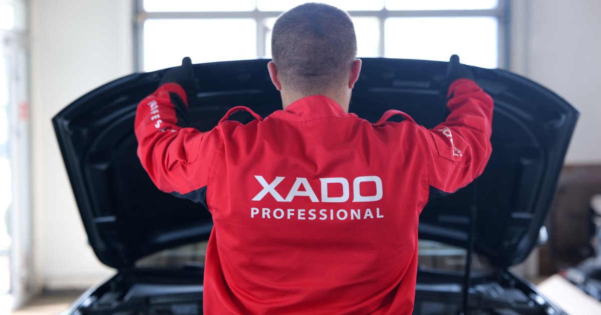 Automotive technician in a professional service uniform inspecting a vehicle with the hood open during maintenance and diagnostics.