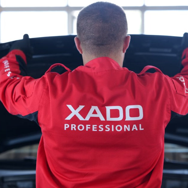 Automotive technician in a professional service uniform inspecting a vehicle with the hood open during maintenance and diagnostics.