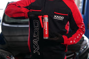 Person in red and black jacket holding a red container with 'XADO' branding.
