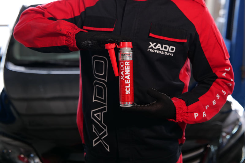 Person in red and black jacket holding a red container with 'XADO' branding.